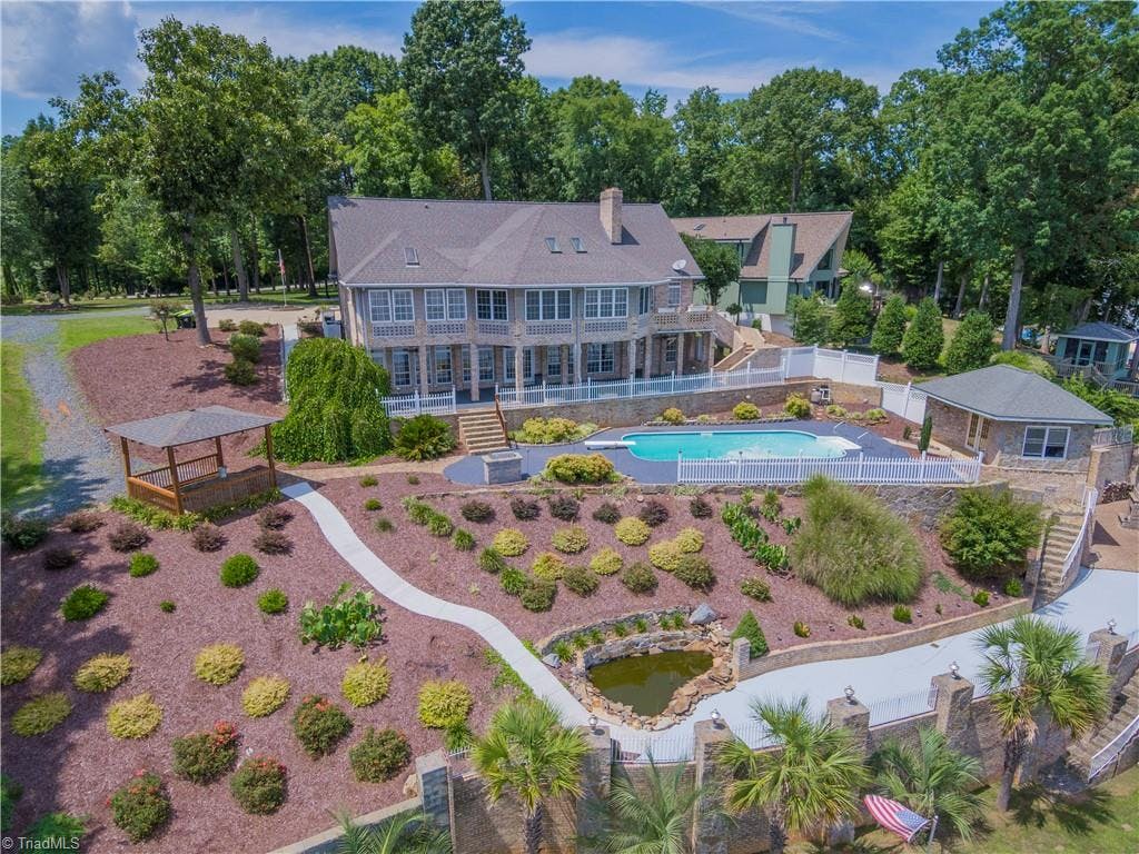 Beautiful landscaping surrounds this lakefront home with inground pool, pool house, outdoor fireplace
