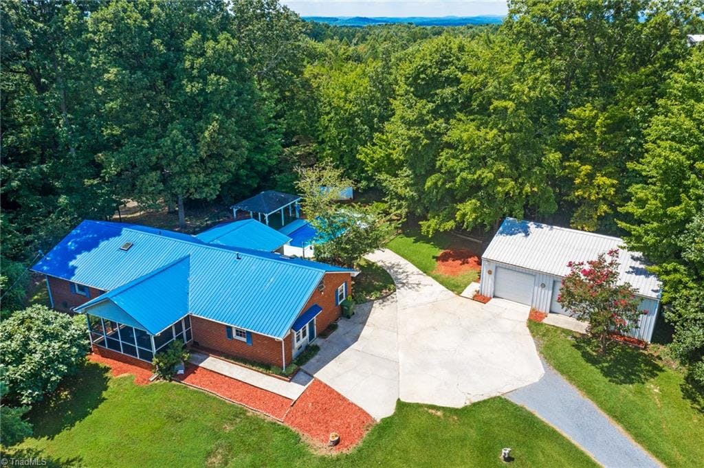 Aerial of home with screened in porch, paved drive, inground pool, 2 car detached garage with a lift.